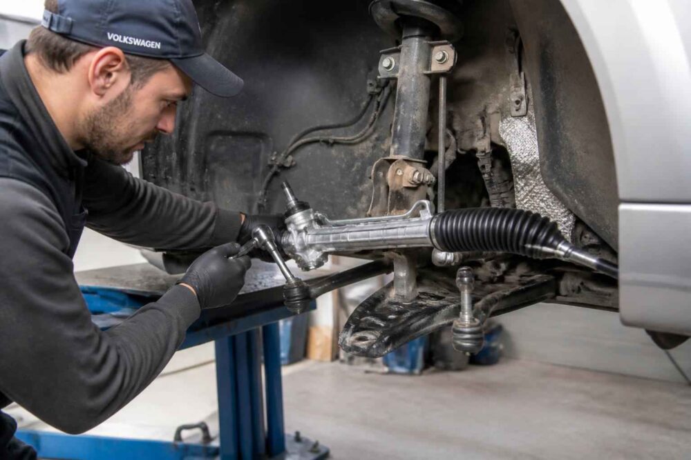 Mechanik w warsztacie naprawia układ kierowniczy samochodu na podnośniku