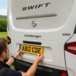 Mężczyzna montuje tylną tablicę rejestracyjną w białym kamperze Swift Challenger 580