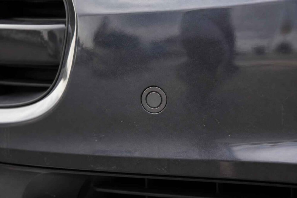 Okrągły sensor w czarnym zderzaku Okrągły czujnik parkowania na czarnym przednim zderzaku obok wlotu powietrza