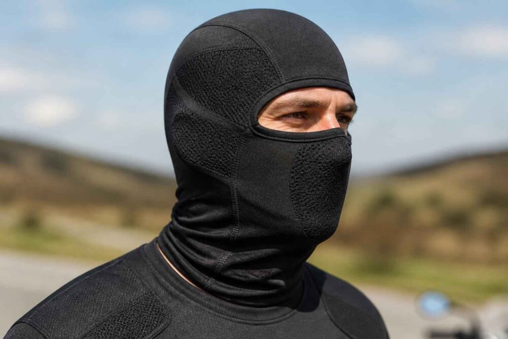 Zamaskowany mężczyzna na górskiej drodze Mężczyzna w czarnej kominiarce i odzieży sportowej na tle pagórkowatego krajobrazu